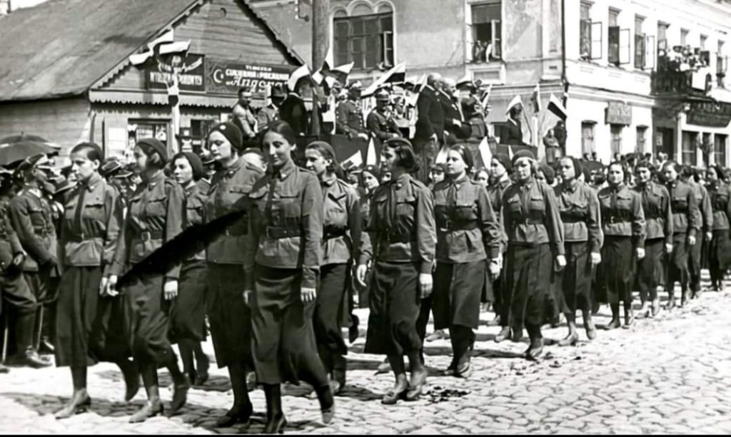 Рівненські гімназистки учасниці воєнізованого формування “Стрілецький союз”. У першій шерензі перша праворуч – рівненська поетка Зюзанна Гінчанка. А ліворуч видніється одноповерхова непримітна будівля, де розмістилась цукерня “Ангора”